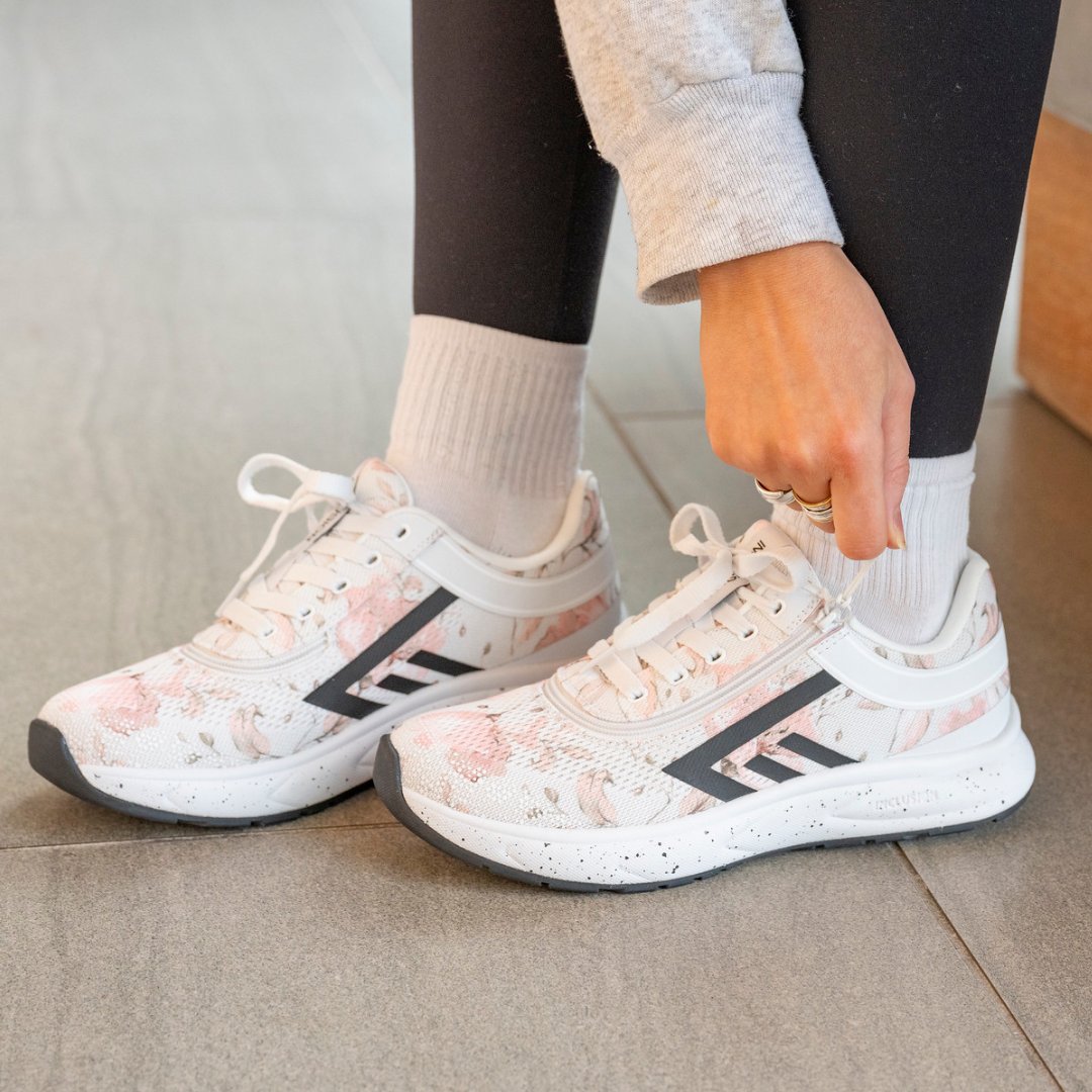 Women's floral athletic shoes in foreground with hand zipping shoes shut.  Wood flooring in background