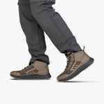 A person wearing gray cargo pants and taupe Men's BILLY Inclusion Trail Boots by BILLY Footwear, featuring an easy on/off zipper, stands against a plain white background.