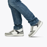 A person in blue jeans and BILLY Footwear Men's White/Grey/Black BILLY Comfort DZ High sneakers is shown walking, one foot lifted off the ground against a plain white background.