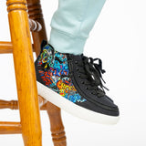 A person in light blue pants stands on a wooden stool, showcasing BILLY Footwear’s Night Sk8ter BILLY Classic D|R II High shoes with graffiti-style artwork on the sides and white soles.